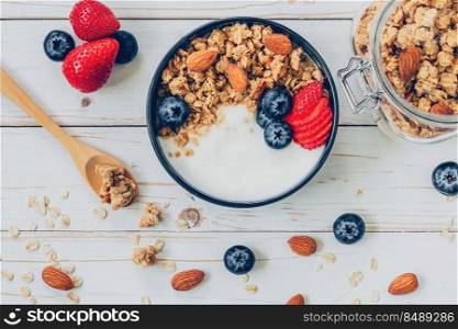 bowl of granola with yogurt, fresh berries, blueberries and nut on wood table.