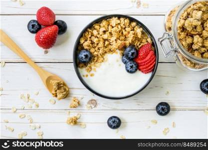 bowl of granola with yogurt, fresh berries, strawberry on wood table.