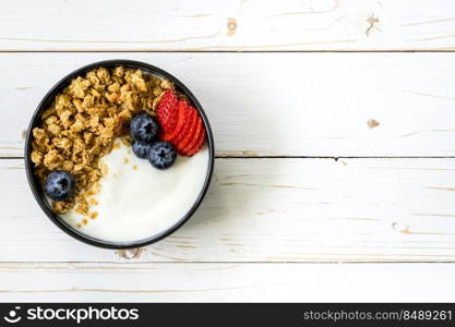 bowl of granola with yogurt, fresh berries, strawberry on wood table.