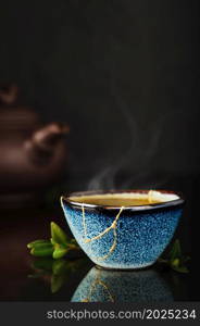 Bowl of green Japanese tea, tea leaves lie next the cup. Selective focus on the cup. Steam rises above the bowl. Reclaimed ceramic blue cup, second life of things, recycling or kintsugi