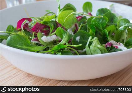 Bowl of green salad with vegetables on a wooden bamboos background