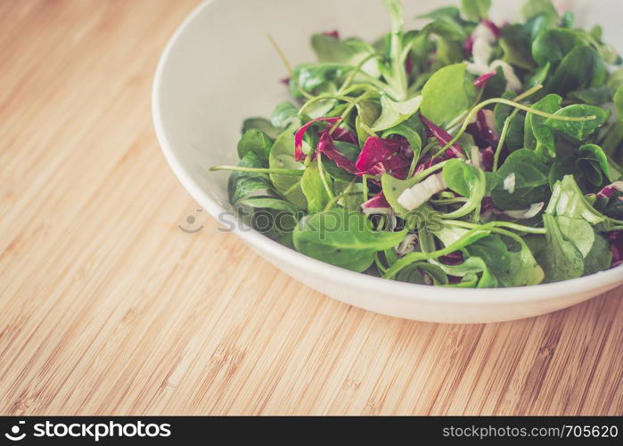 Bowl of green salad with vegetables on a wooden bamboos background