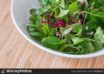Bowl of green salad with vegetables on a wooden bamboos background