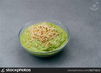 Bowl of green smoothie made of spinach with buckwheat sprouts on grey background. Vegan food. Healthy eating and nutrition concept