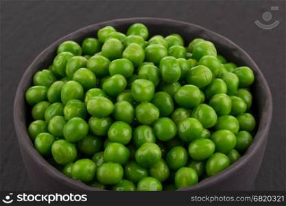 Bowl of green wet pea isolated on dark stone background
