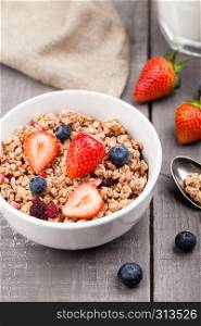 Bowl of healthy cereal granola with strawberries and blueberries and glass of milk on wooden board