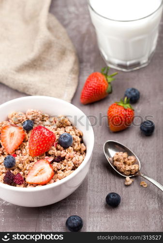 Bowl of healthy cereal granola with strawberries and blueberries and glass of milk on wooden board