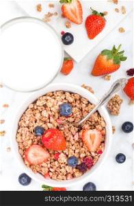 Bowl of healthy cereal granola with strawberries and blueberries and glass of milk on marble board