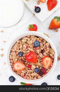 Bowl of healthy cereal granola with strawberries and blueberries and glass of milk on marble board