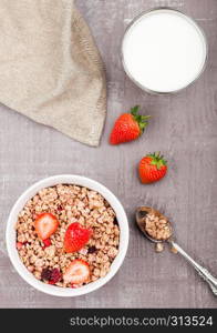 Bowl of healthy cereal granola with strawberries and glass of milk on wooden board