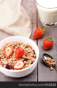 Bowl of healthy cereal granola with strawberries and glass of milk on wooden board