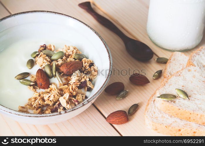 Bowl of homemade granola, almond and yogurt, milk and whole wheat bread on wooden table. Healthy concept