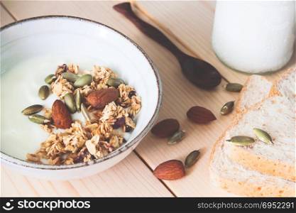 Bowl of homemade granola, almond and yogurt, milk and whole wheat bread on wooden table. Healthy concept