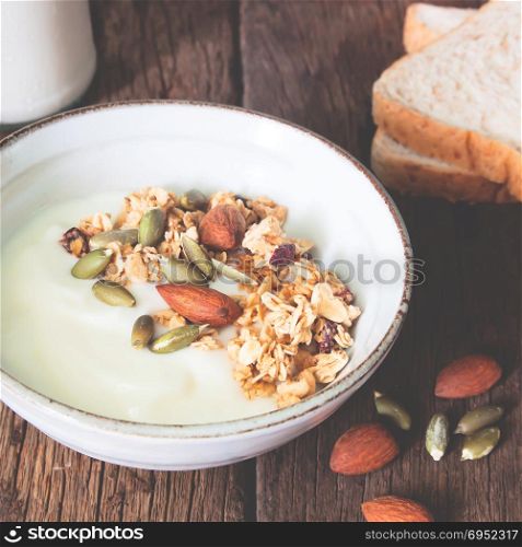 Bowl of homemade granola with yogurt and almond on wooden table
