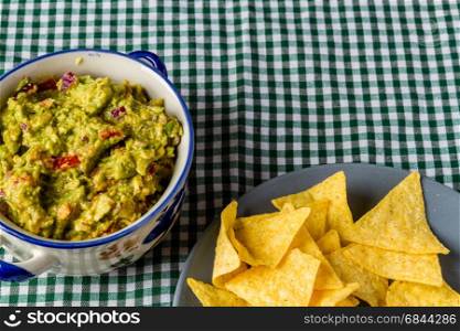 Bowl of homemade guacamole, ready for eating with tortilla chips on the side.