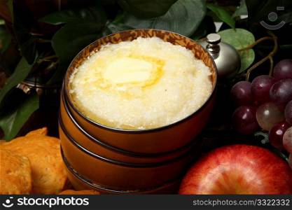 Bowl of hot grits and butter with biscuits and fruit in kitchen.