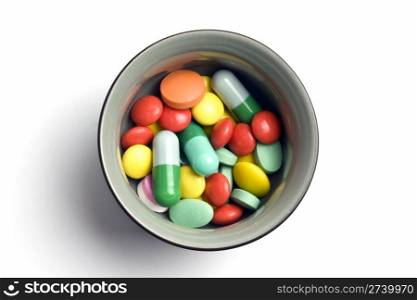 Bowl of multicolored tablets and capsules isolated on white