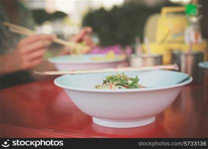 Bowl of noodles outside by the street with a woman in the background