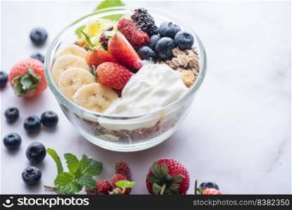 bowl of oat granola with yogurt, fresh blueberries, mulberry, strawberries, kiwi, banana, mint and nuts board for healthy breakfast, top view, copy space, flat lay. vegetarian food concept.