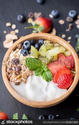 bowl of oat granola with yogurt, fresh blueberries, strawberries, kiwi mint and nuts board for healthy breakfast,  Healthy breakfast menu concept. On the black rock