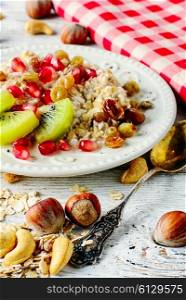 Bowl of oatmeal with slices of kiwi and pomegranate and scattered the table with hazel and cashew nuts. Dish of oat flakes