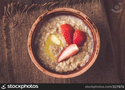 Bowl of oats with fresh strawberries on the wooden table