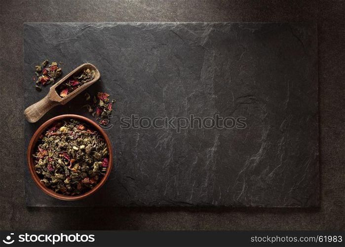 bowl of of dry tea and scoop at slate background
