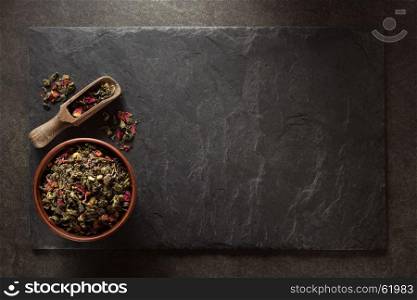 bowl of of dry tea and scoop at slate background