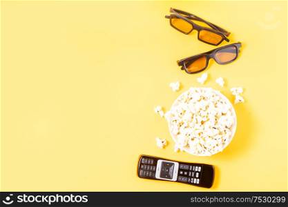 bowl of popcorn, nd remote control for TV and 3d glasses over yellow background with copy space, movie and cinema concept. popcorn and 3d glasses
