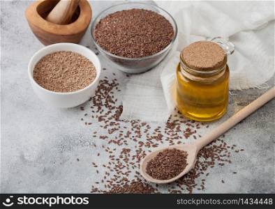 Bowl of raw natural organic linseed flax-seed with spoon and glass jar oil on light background with linen cloth. Mixed seeds powder in white bowl.