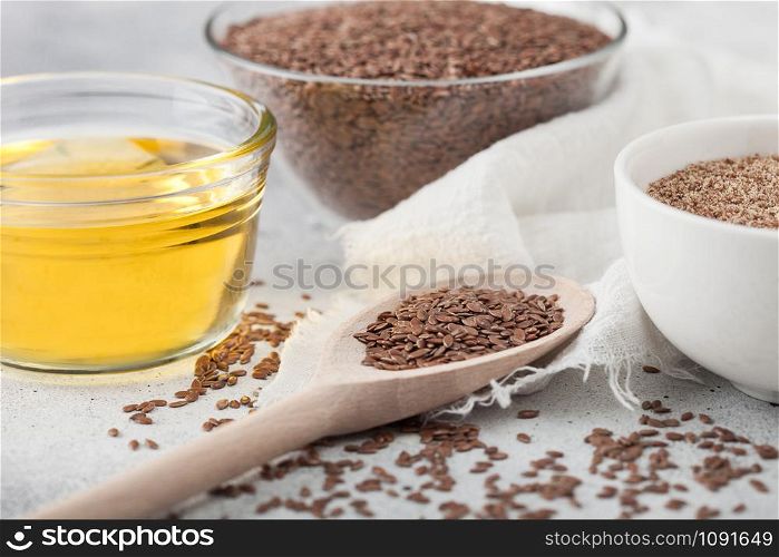 Bowl of raw natural organic linseed flax-seed with spoon and oil on light background with linen cloth.