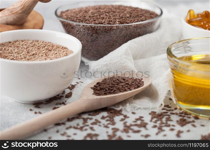 Bowl of raw natural organic linseed flax-seed with spoon and oil on light background with linen cloth.