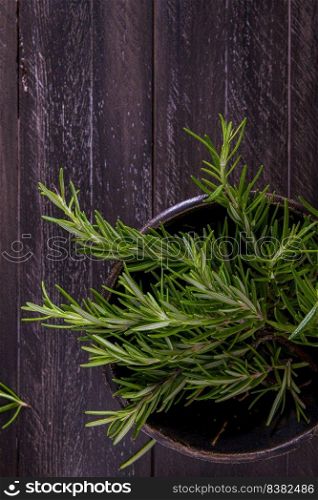Bowl of rosemary on wooden background, top view.