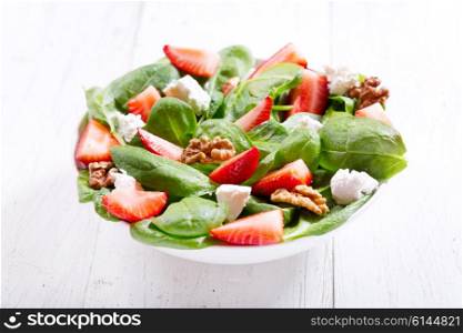 bowl of salad with strawberry, spinach leaves and feta cheese on wooden table