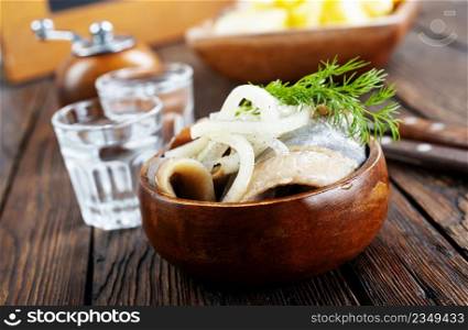 bowl of salted herring on the background of a glass of vodka and decanter. Salted herring in jar as a snack for vodka.