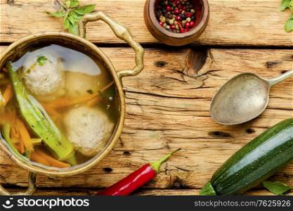 Bowl of soup with meatballs and vegetables on retro wooden table.Soup with zucchini and meatballs. Soup with meat balls and vegetables