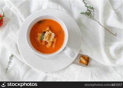 Bowl of tomato soup with croutons and fresh thyme on white background.