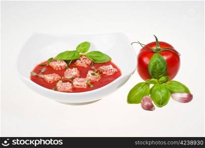 Bowl of tomato soup with tomato, basil and garlic over white background