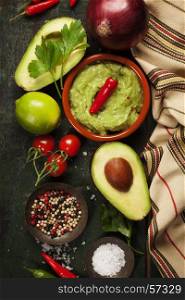 Bowl of Traditional latinamerican mexican sauce guacamole with fresh ingredients on dark rustic background. Top view