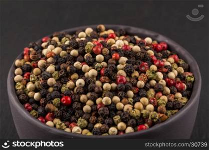 bowl of various pepper peppercorns seeds mix on dark stone