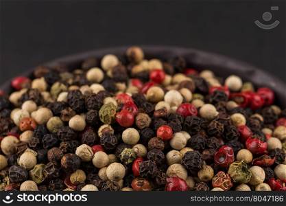 bowl of various pepper peppercorns seeds mix on dark stone