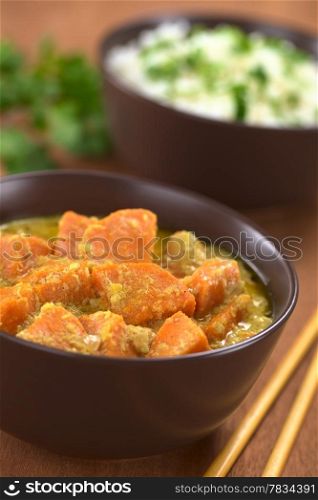 Bowl of vegetarian sweet potato and coconut curry with cooked rice in the back (Selective Focus, Focus one third into the curry). Sweet Potato and Coconut Curry