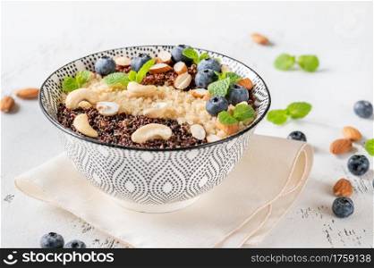 Bowl of white, red and black cooked quinoa with nuts and blueberries