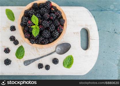 Bowl with and blackberries and mint leaves on a old wooden background