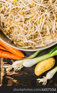 Bowl with bean sprouts and soybean sprouts with fresh organic vegetables on rustic wooden background, top view, close up.