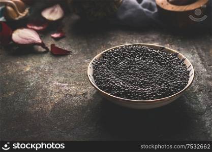 Bowl with black lentil standing on dark rustic kitchen table background with ingredients. Close up. Copy space. Healthy food. Protein rich vegan foods. Plant based protein source