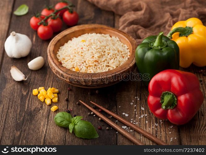 Bowl with boiled long grain basmati vegetable rice on wooden background with sticks and paprika pepper with corn,garlic and basil and tomatoes.