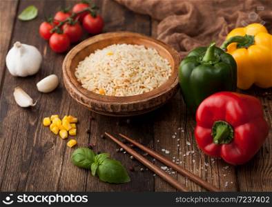 Bowl with boiled long grain basmati vegetable rice on wooden background with sticks and paprika pepper with corn,garlic and basil and tomatoes.