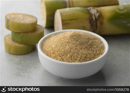 Bowl with cane sugar and fresh sugar cane in the background