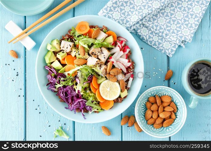 Bowl with grilled chicken meat, brown rice and fresh vegetable salad of avocado, radish, cabbage kale, carrot, and lettuce leaves. Healthy and delicious dietary lunch. Top view